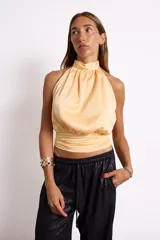 Blusa color amarillo pálido con cuello halter y corte irregular en la cintura.