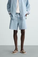 Shorts de denim de algodón, color celeste lavado, de corte regular fit y largo hasta la rodilla. Presenta cierre frontal con cremallera y botón, bolsillos delanteros y bolsillos traseros de plastrón. El borde inferior tiene un acabado deshilachado.