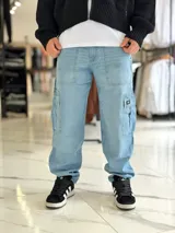 Pantalón cargo de jean azul claro, con bolsillos laterales tipo cargo en las piernas y bolsillos frontales aplicados, de corte ancho y holgado.