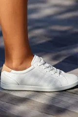 Zapatillas deportivas blancas de cuero, estilo casual de caña baja con cordones. Presentan perforaciones horizontales en el lateral y un detalle de cuero color camel en el talón.