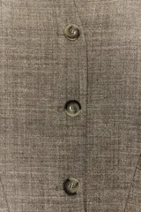 Chaqueta corta de corte estructurado confeccionada en tejido con mezcla de lana. Presenta cuello en pico, cierre frontal con botones y mangas largas. El diseño incluye bolsillos delanteros y un forro interior a contraste.