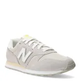 Championes urbanos New Balance modelo 373, confeccionados en una combinación de gamuza y malla en tonos gris claro y beige. Presentan el logo 'N' característico en los laterales, cierre con cordones y suela de goma con entresuela amortiguada.