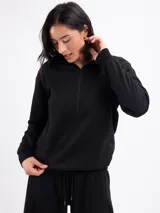 Buzo de felpa color negro con cuello alto y cierre frontal parcial, de manga larga con puños elásticos y diseño holgado.