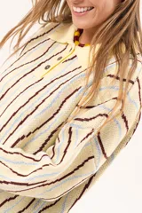Buzo de punto tipo polo en tono amarillo claro con diseño de ondas a rayas en tonos marrón y celeste. Presenta cuello clásico, cierre frontal parcial con botones y silueta relajada con mangas largas.