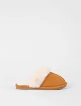 Pantufla tipo mule color tostado con exterior de material suave y forro interior de corderito sintético color crema. Cuenta con suela plana de goma.