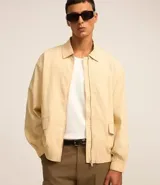 Campera color beige claro de algodón con textura arrugada, cuello inglés, cierre con cremallera, bolsillos laterales, elástico en la cintura y puños.