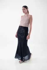 Vestido largo de fiesta con lentejuelas, compuesto por un top verde esmeralda con cuello halter y una falda negra ajustada con abertura lateral.