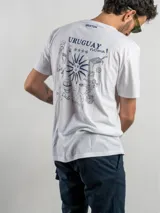 Remera blanca de corte regular con estampado gráfico en la espalda que incluye elementos icónicos de la cultura uruguaya como el sol, un tambor, una parrilla y frases alusivas. Cuenta con cuello redondo y mangas cortas.