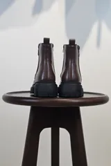 Bota de caña corta color marrón, con cierre lateral y suela track negra de goma con plataforma.