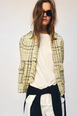 Chaqueta de corte recto confeccionada en tejido con textura de cuadros en tonos amarillos, blancos y negros. Presenta cuello solapa, cierre frontal con botones ocultos, bolsillos de plastrón con solapa en el delantero y mangas largas con puños abotonados.