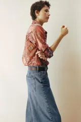 Camisa de manga larga confeccionada en gasa de algodón con estampado tipo paisley y motivos ornamentales en tonos rojizos y rosados. Presenta cuello clásico, cierre frontal con botones y puños abotonados.