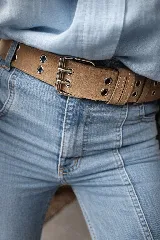 Cinturón de gamuza color camel con doble hebilla metálica plateada y múltiples ojales metálicos a lo largo de la tira.