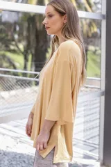 Remera de corte holgado con mangas anchas y aberturas laterales en el ruedo. Presenta un estampado floral pequeño en tonos violeta y verde sobre una base blanca con textura acanalada.