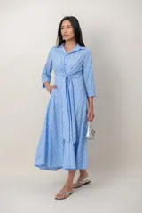 Vestido midi celeste con diseño de rayas blancas, cuello camisero, mangas 3/4 y un lazo ajustable en el frente con nudo.