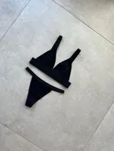 Conjunto de ropa interior compuesto por un bralette sin taza y una bombacha tipo less, confeccionados en algodón y lycra. El diseño presenta elásticos personalizados con el nombre de la marca en la banda inferior del bralette, los breteles y la cintura de la bombacha.