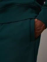 Pantalón de chándal verde oscuro de felpa gruesa con cintura y puños elásticos, bolsillos laterales y traseros, corte recto y holgado. Con bordado de Calvin Klein en la cadera.