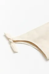 Bombacha de bikini tipo vedetina color beige, con textura arrugada y lazos laterales ajustables.