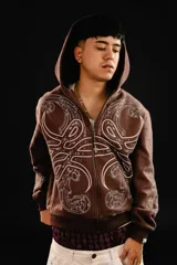 Hoodie con cierre frontal, color marrón, con diseño estampado de hojas de acanto en color blanco que recorre el frente y las mangas. Cuenta con bolsillos laterales y costuras visibles.