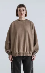 Buzo de cuello redondo color marrón claro, confeccionado en algodón premium con textura acanalada. Presenta costuras expuestas y detalles deshilachados en cuello, puños y ruedo, con un calce oversize y mangas abullonadas.