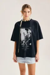 Remera oversize de algodón negro, con cuello redondo y mangas cortas. Presenta un estampado gráfico frontal en blanco y negro de estilo vintage.