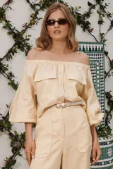 Blusa color amarillo claro, con escote off-shoulder, mangas largas abullonadas y dos bolsillos con solapa en el pecho.