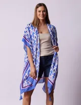 Kimono tejido con estampado abstracto en tonos azules, blancos y violetas. Tiene terminación de ruedo con borlas.