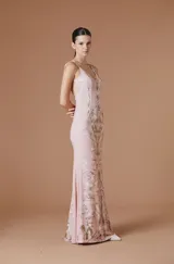 Vestido largo de Natalia Antolin con escote en V y breteles finos. Presenta un diseño ajustado en el torso que se ensancha suavemente hacia el ruedo, con un estampado botánico simétrico en tonos tierra sobre una base rosada.