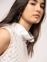 Blusa blanca sin mangas, con cuello alto con volados y detalles bordados con motivos florales.