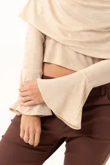 Blusa beige con hombros descubiertos, confeccionada en tela elástica con destellos de lurex. Presenta mangas largas con terminación acampanada y diseño ajustado al cuerpo.