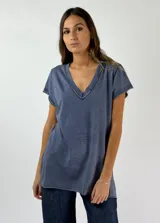 Remera azul de corte recto con cuello en V y detalle de tachas plateadas en el borde del escote.