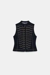 Chaleco de denim azul oscuro con cuello redondo y cierre frontal de botones. Presenta un diseño de pespuntes decorativos en contraste con forma de alamares en la parte delantera.