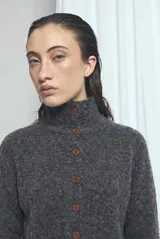 Cardigan de punto color gris oscuro melange, con cuello alto, mangas largas y cierre frontal con botones marrones.