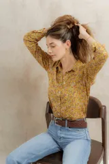 Camisa de corte clásico con cuello camisero y cierre frontal de botones, confeccionada en tela con estampado floreado en tonos amarillos, rosas y blancos.