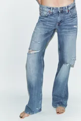 Jeans de tiro bajo y cinco bolsillos, con diseño de pierna ancha y larga. Presenta roturas y desgastes sutiles en la parte delantera. Cierre frontal con cremallera y botón metálico.