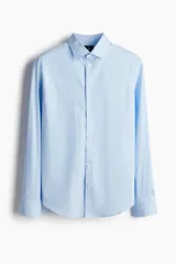 Camisa de manga larga color celeste claro, con cuello italiano y tapeta lisa con botones blancos. Presenta un corte ajustado (slim fit) y bajo redondeado.