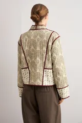 Chaqueta capitoneada de diseño acolchado con estampado paisley en tonos beige y verde, con ribetes y lazos de cierre frontales en color bordó.