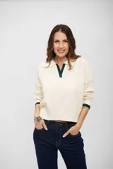 Buzo de tejido de punto color crema con cuello polo y detalles en color verde oscuro en el cuello y los puños. Presenta un diseño de manga larga con textura acanalada en los antebrazos y corte recto.