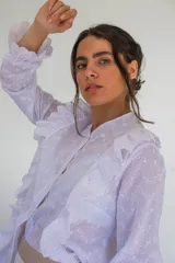 Camisa blanca de algodón estilo romántico con tejido broderie, mangas largas con puños volados y detalles de volados frontales.