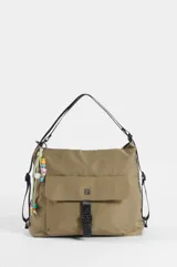 Mochila hobo color marrón claro, convertible en cartera de hombro, confeccionada en nylon. Cuenta con un compartimento principal con cierre, un bolsillo frontal con solapa y cierre de botón a presión, tiras regulables negras y un llavero colgante decorativo con cuentas coloridas y borla.