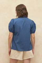 Camisa roja con cuello clásico, mangas cortas abullonadas y cierre frontal con botones.