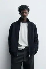 Chaqueta regular fit de cuello subido, confeccionada en tejido técnico interlock de algodón con elasticidad. Presenta cierre frontal con cremallera, manga larga con puños en rib y bolsillos de vivo en la cadera.