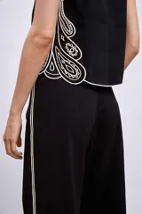 Blusa negra sin mangas, de corte recto y escote redondo, con detalles de bordados contrastantes en color blanco en los bordes y costados.