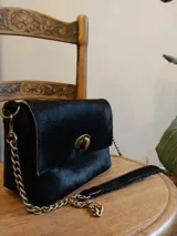 Cartera bandolera negra de cuero con pelo, cierre dorado y correa de cadena dorada.