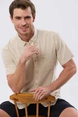 Camisa de manga corta confeccionada en mezcla de lino y algodón, color beige, con cuello camisero abotonado, bolsillo frontal en el pecho y cierre de botones.