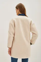 Saco de corte recto confeccionado en tejido tipo boucle color crema, con terminaciones en contraste color marrón y cierre frontal con botones metálicos.
