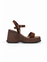 Sandalia de plataforma con taco corrido y textura simil piel de reptil, en color marrón chocolate. Cuenta con tiras delanteras de gamuza y tira ajustable al tobillo con hebilla metálica.