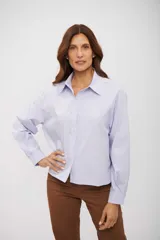 Camisa de vestir holgada, color celeste claro, con finas rayas verticales blancas y detalles de lentejuelas blancas dispersas por toda la prenda. Posee cuello camisero y cierre frontal de botones.