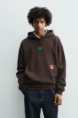 Sudadera con capucha de corte relajado, color marrón oscuro, con interior perchado. Presenta un bolsillo frontal tipo canguro, bordado con la palabra 'LOVE' en el pecho y un parche decorativo a contraste en el bolsillo. Posee puños y ruedo en rib.