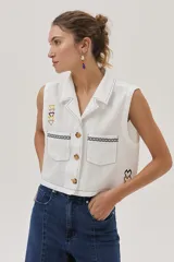 Blusa blanca de lino con cuello camisero, sin mangas, cierre frontal con botones y bordados en el frente.