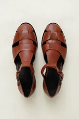 Sandalia cerrada tipo pescador, color blanco o hueso brillante, con tiras entrecruzadas en el empeine y cierre de hebilla ajustable en el lateral. Posee suela y taco bajo de color negro.